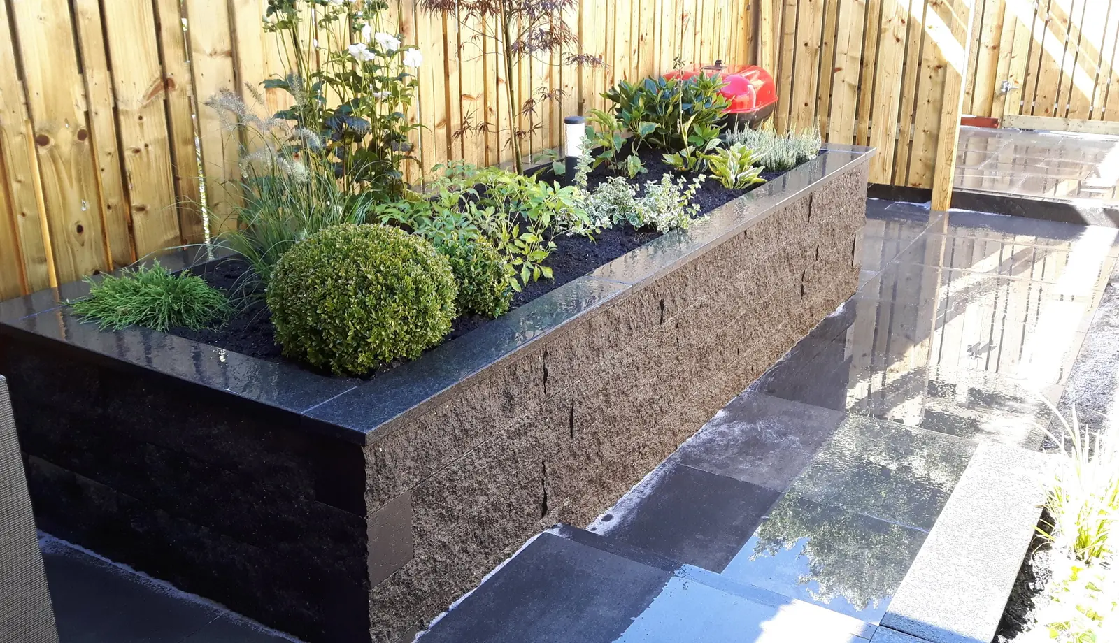 Houten schutting met verhoogde plantenbak en bestrating